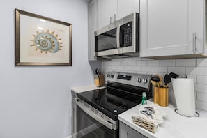 Eine Küche mit weißen Schränken, einem Edelstahlbackofen, einer Mikrowelle und einem gerahmten Kunstwerk an der Wand.