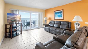 A living room with a sofa, a television, and a balcony with a view. - Beach Front 3 Bedroom - Beach Place #507 (Madeira Beach)