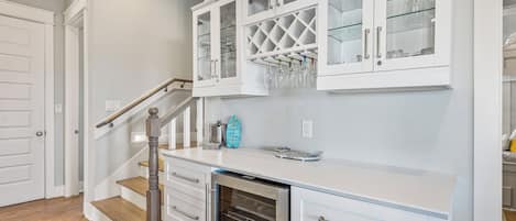 A kitchen with white cabinetry, a stainless steel dishwasher, and a glass wine rack.