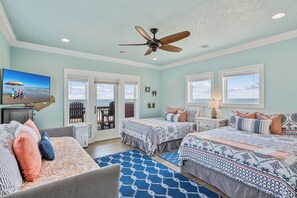 Une chambre avec deux lits, un ventilateur de plafond et une vue sur la plage par les fenêtres.