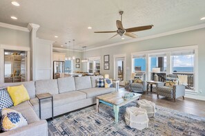A spacious living room with a large sofa, a coffee table, and a ceiling fan. - Easy Breezy! 4 bedroom 4 Bath, Direct Ocean view, easy beach access. (Crystal Beach)