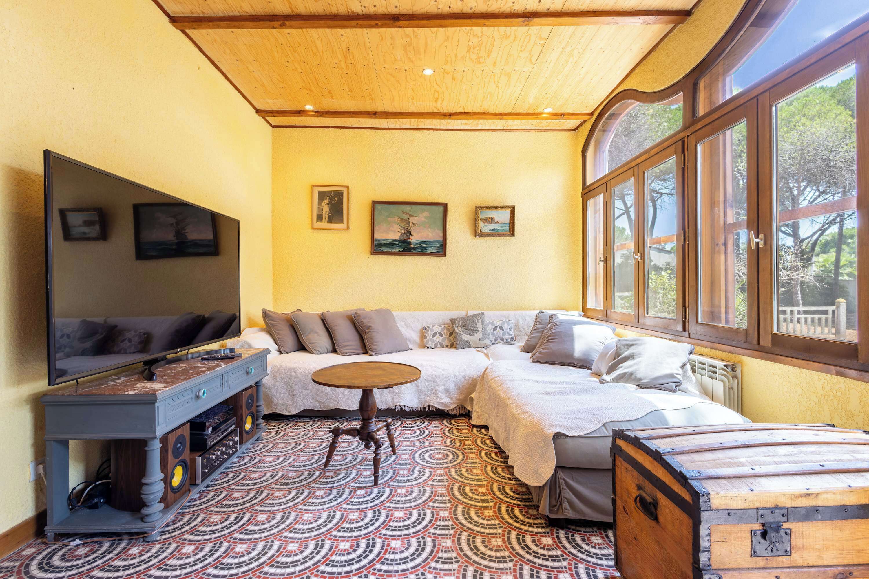 Una habitación acogedora con un sofá, una mesita redonda y un televisor. Hay tres cuadros enmarcados en la pared.