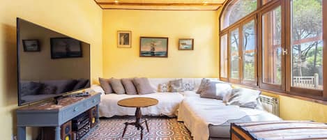 A cozy room with a sofa, a small round table, and a television. There are three framed pictures on the wall.