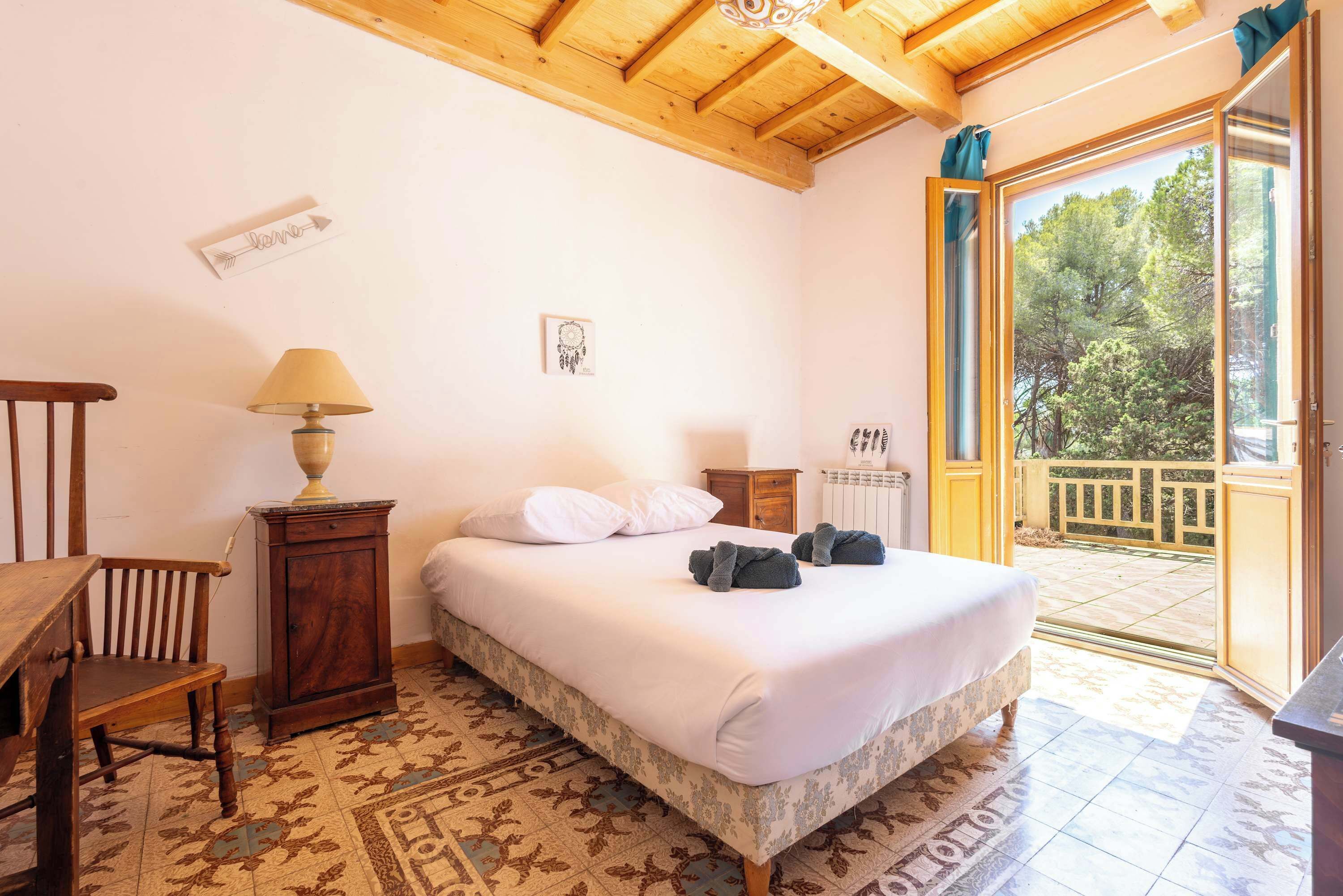 Une chambre à coucher comprenant un lit, une table de chevet, une lampe, une chaise et une vue sur l’extérieur grâce à une porte vitrée.