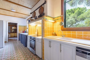 A kitchen with a tiled backsplash, a window with a view of trees, and a dishwasher. - La villa  des pins (Agde)