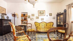 A traditional living room with patterned floor tiles, a floral sofa, wooden chairs, a bookshelf, and framed pictures on the walls. - La villa  des pins (Agde)