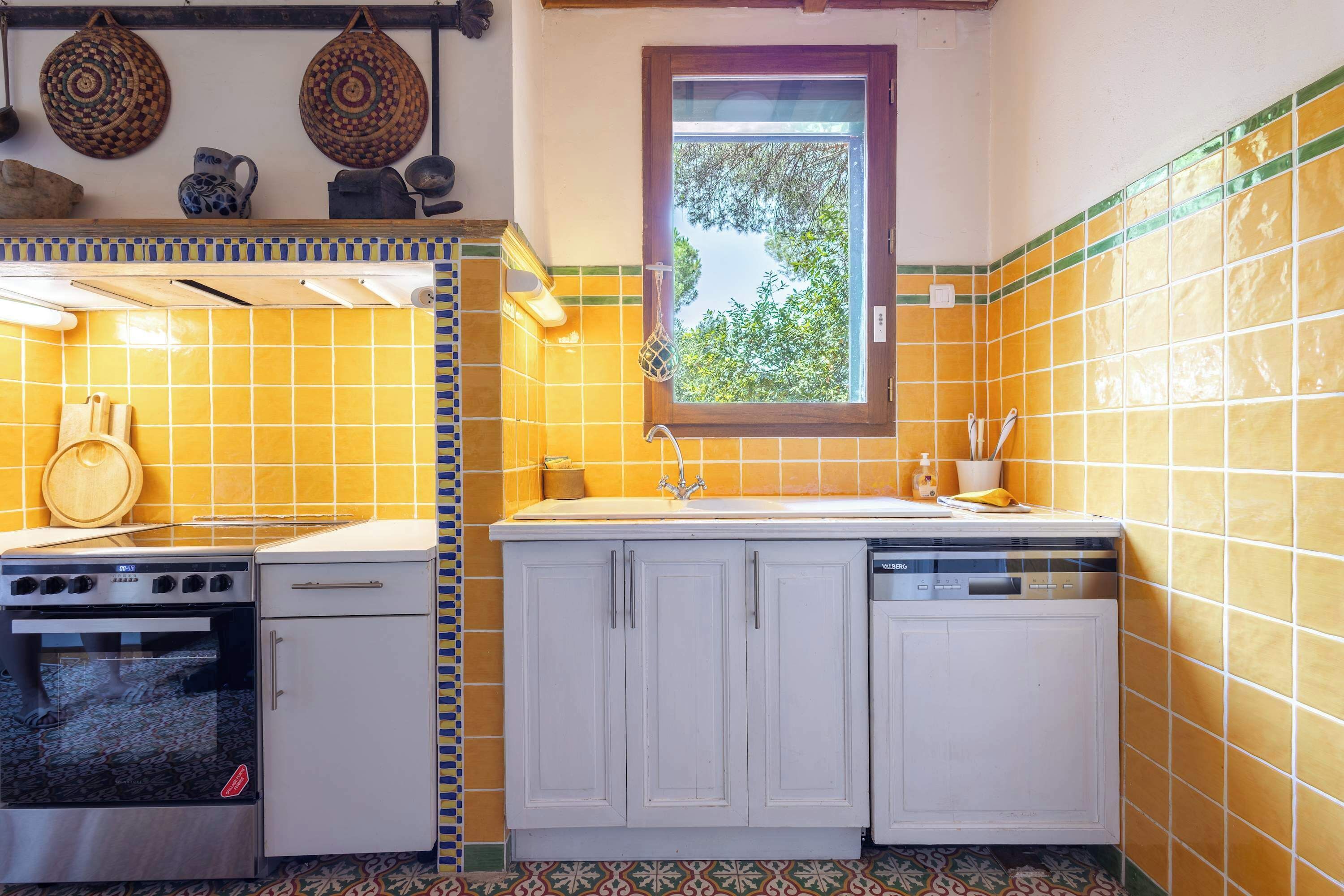 A compact kitchen with a stove, oven, and dishwasher. There is a window with a view of trees.