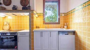 A compact kitchen with a stove, oven, and dishwasher. There is a window with a view of trees.
