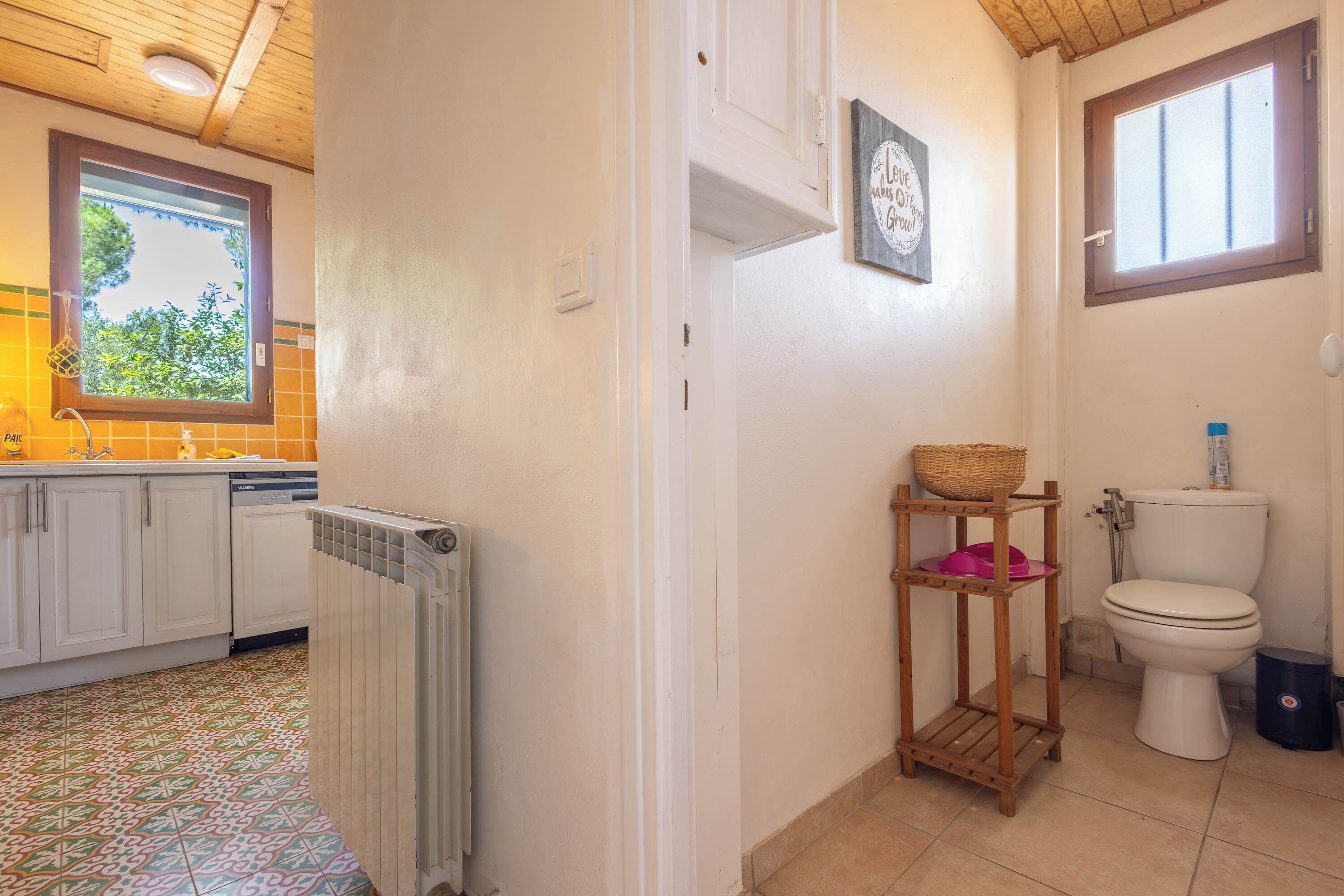 Une salle de bain avec des toilettes, une petite étagère en bois sur laquelle se trouve un panier, et une fenêtre.