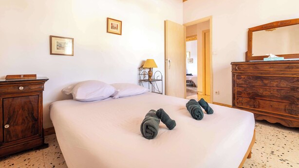 A bedroom with a bed, a wooden dresser, a nightstand, and a lamp. - La villa  des pins (Agde)