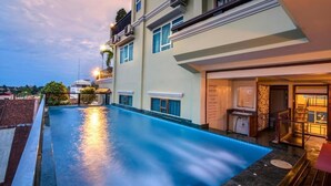 A modern hotel with a rooftop infinity pool, a covered outdoor area, and a well-lit entrance.
