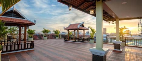 A rooftop terrace with tiled flooring, traditional-style pavilions, and a view of the city skyline.