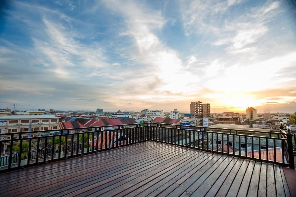 Una terraza de madera con barandal negro que da a una vista panorámica de la ciudad al atardecer.