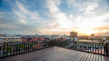 Una terraza de madera con barandal negro que da a una vista panorámica de la ciudad al atardecer.