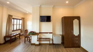 A room with a wooden bench, a small table with flowers, a television mounted on the wall, and a wardrobe.