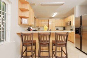 A kitchen with wooden cabinets, a stainless steel refrigerator, and three wooden bar stools. - 4 BR w/ 6 Beds Near Atlantis (Nassau)