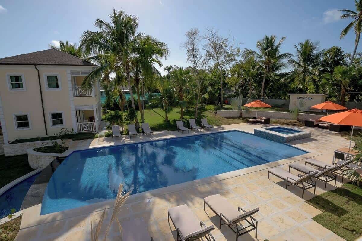 Piscina com espreguiçadeiras, palmeiras e um edifício com varandas.