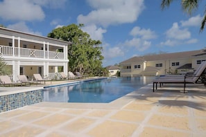 A pool area with lounge chairs, a two-story building with balconies, and a clear sky. - 4 BR w/ 6 Beds Near Atlantis (Nassau)