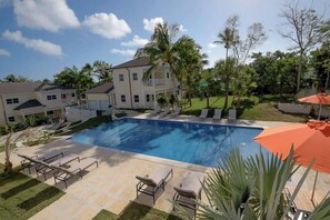 A swimming pool with lounge chairs, a large house, and surrounding greenery.