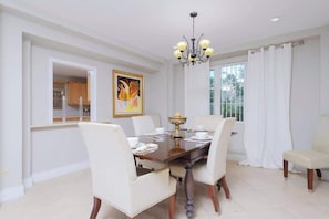 A dining room with a chandelier, a dining table set for four, and a painting on the wall.