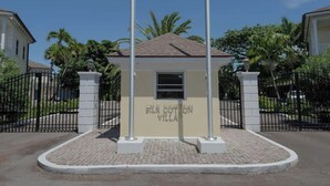 Un petit bâtiment, portant l’inscription « Villa Silk Cotton », avec un toit en tuiles, entouré d’une zone pavée en briques et d’une clôture en métal noir.