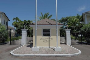 A small building labeled 'Silk Cotton Villa' with a tiled roof, surrounded by a brick-paved area and black metal fencing. - 4 BR w/ 6 Beds Near Atlantis (Nassau)