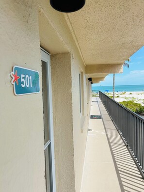 A corridor with a balcony overlooking a beach, a sign indicating room number 501, and a clear view of the ocean. - Beautifully Remodeled Gulf View Condo on Sanibel Island (Sanibel)