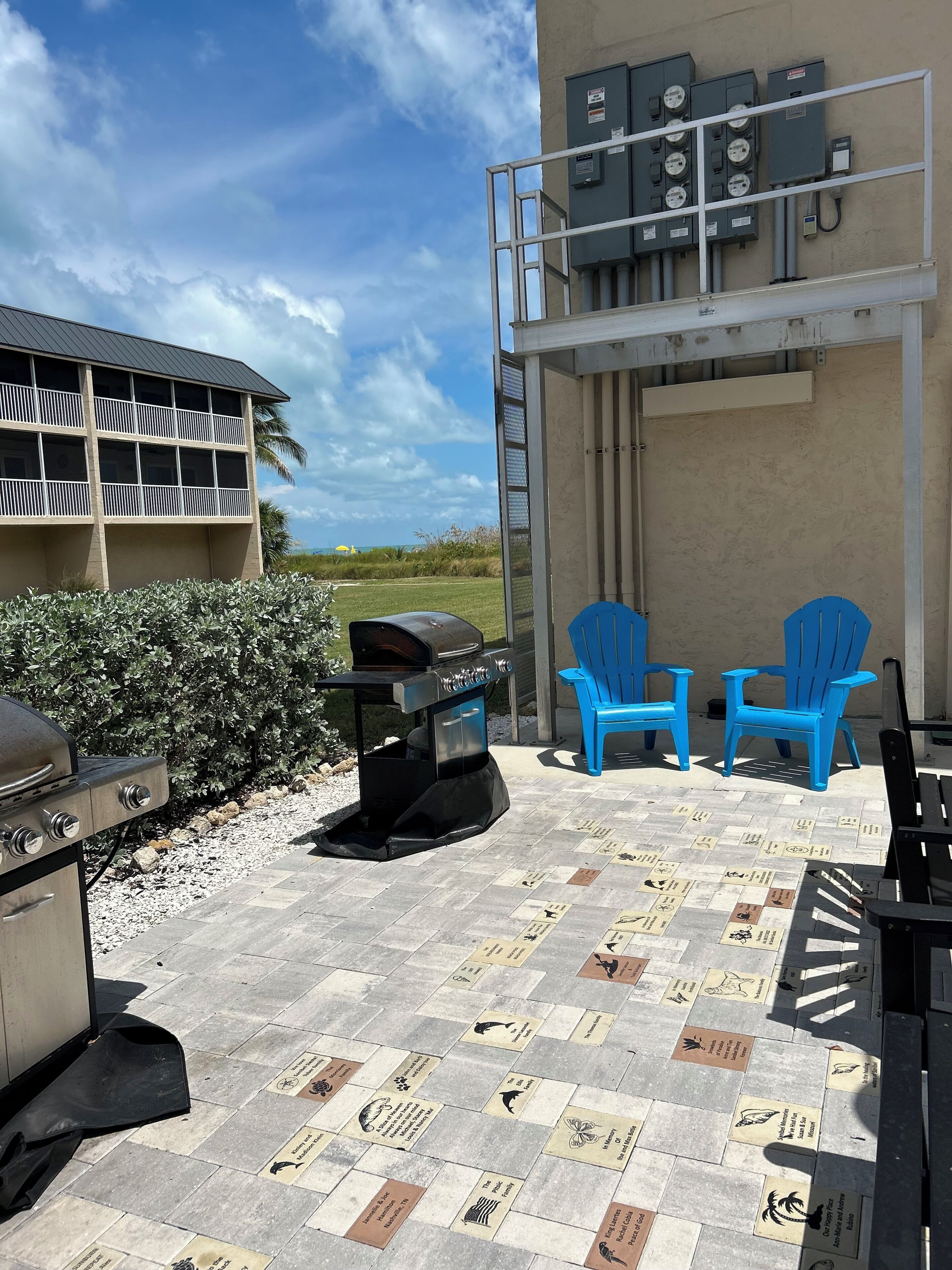 An outdoor patio with a grill, blue chairs, and a view of the ocean.