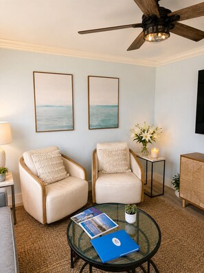A living room with two armchairs, a coffee table with magazines, a ceiling fan, and artwork on the wall. - Beautifully Remodeled Gulf View Condo on Sanibel Island (Sanibel)