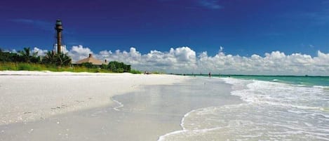 A beach with a lighthouse, clear sky, and calm sea.