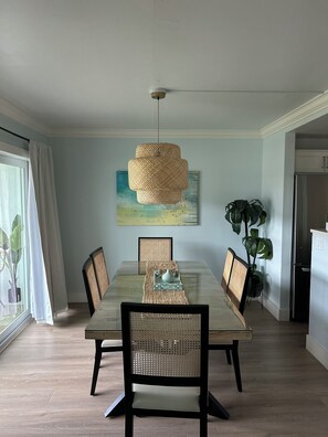 Ein Esszimmer mit Holztisch, gewobenen Stühlen, einer Pendelleuchte und einem Bild an der Wand.