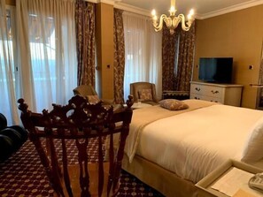 A hotel room with a large bed, a wooden chair, a television, and curtains.