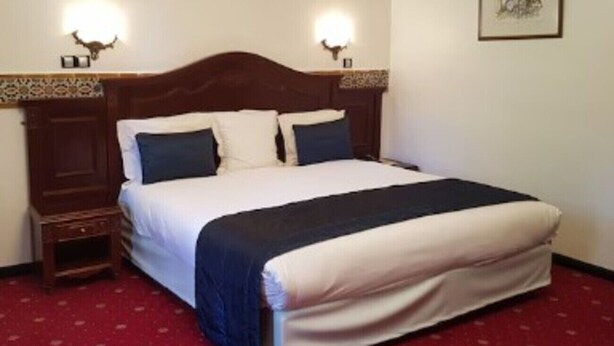 Habitación de hotel con una cama individual, dos mesitas de noche y una lámpara fijada a la pared.