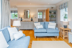 A living room with a blue sofa set, a wooden coffee table, and a side table with a lamp. - Pebbles, Thornham, Norfolk (Thornham)