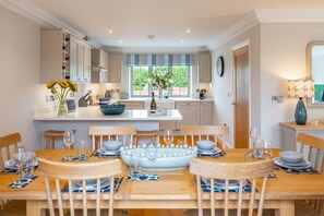 A modern kitchen with a central island, wooden chairs, and a dining table set for six. - Pebbles, Thornham, Norfolk (Thornham)
