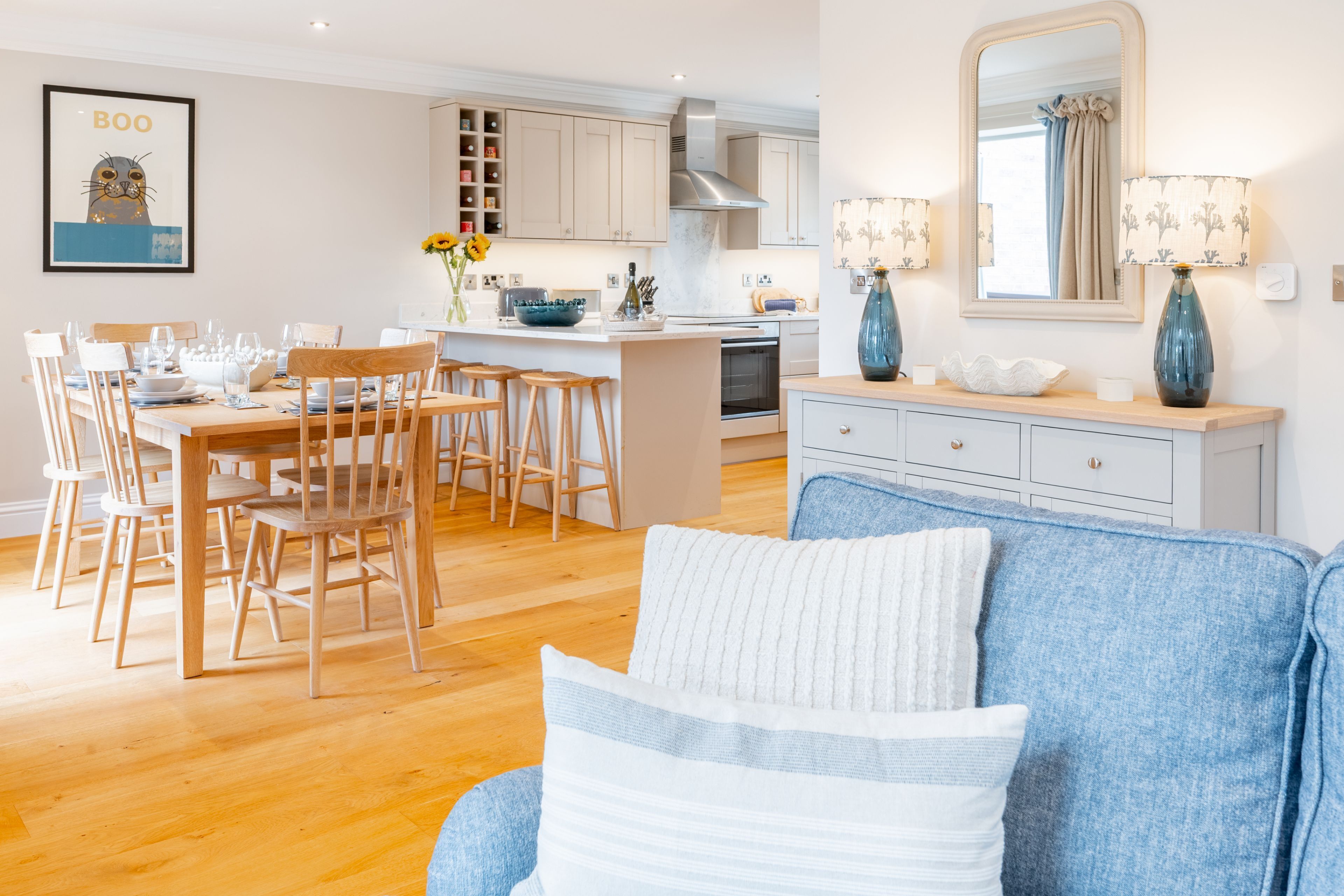 A modern kitchen with white cabinets, a dining area with wooden chairs, and a blue sofa with white cushions.