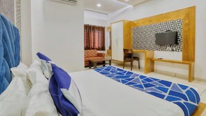 Habitación de hotel con cama, televisión montada en un panel de madera, escritorio y sofá.
