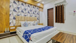 Habitación de hotel con cama, cabecero de madera, pared con diseño geométrico, unidad de aire acondicionado, puerta marrón y una pequeña mesa de madera.
