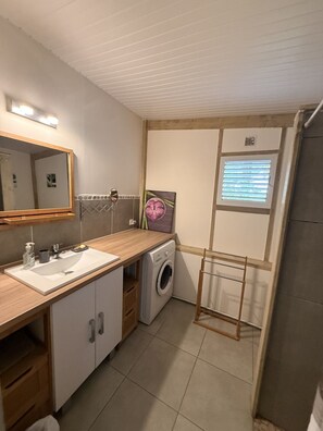 Ett litet badrum med dubbelt handfat, en spegel, en tvättmaskin och ett torkställ.