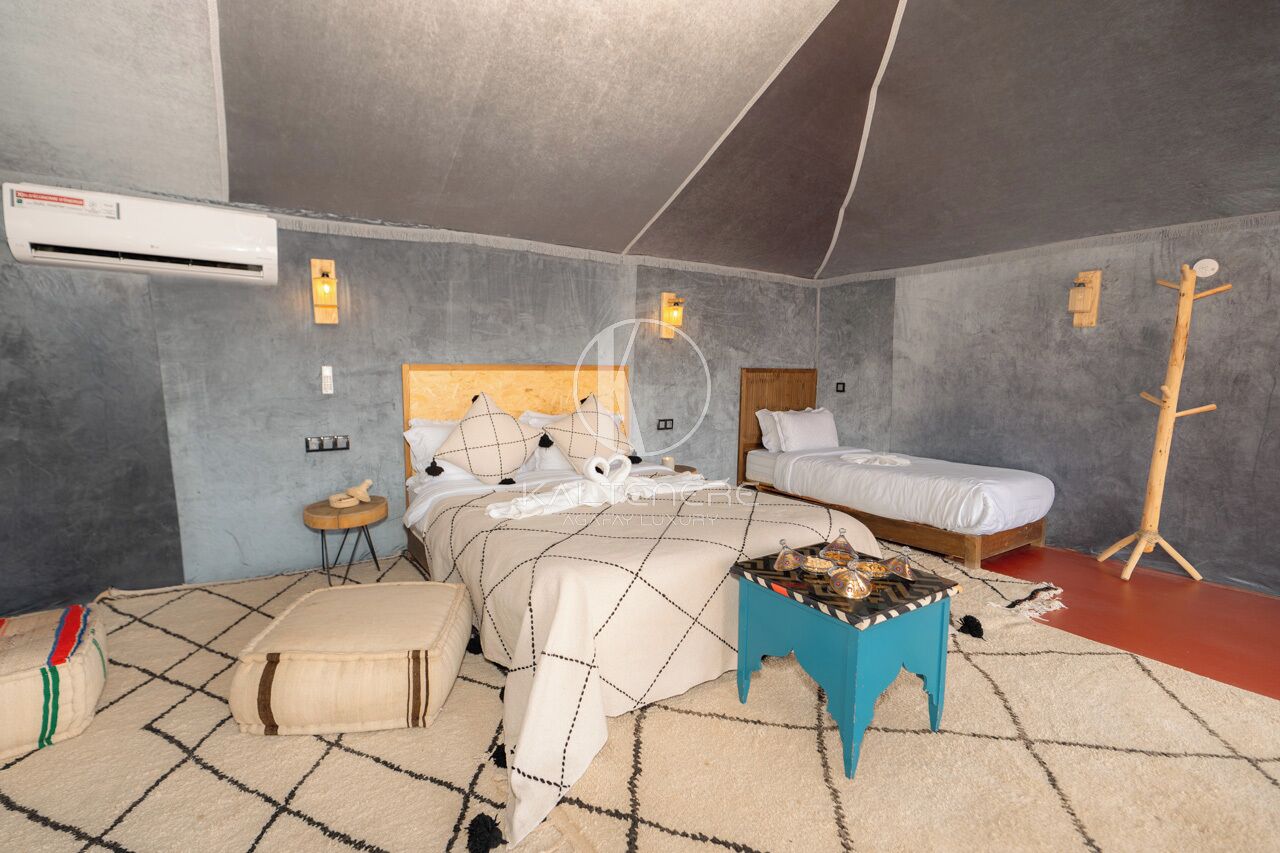Un dormitorio con cama, mesitas de noche, un taburete pequeño y un equipo de aire acondicionado.