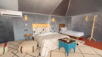 Un dormitorio con cama, mesitas de noche, un taburete pequeño y un equipo de aire acondicionado.