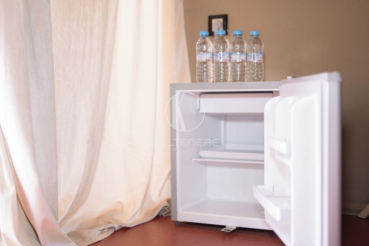 A white mini-fridge with a water bottle holder on top, positioned next to a curtain.