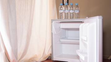 A white mini-fridge with a water bottle holder on top, positioned next to a curtain.