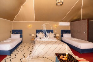 A room with two beds, a large bed with a decorative headboard, and a smaller bed. There are wall-mounted lights and an air conditioning unit. - Kal Tenere Luxury Camp (Agafay)