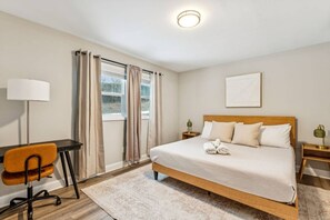 A hotel room with a bed, a desk, an orange chair, a lamp, and a window with curtains. - Modern & Cozy Oasis In Noda | Community Gym, Dog Park & Courtyard with Firepit | Pets OK! +20% Off! (Charlotte)