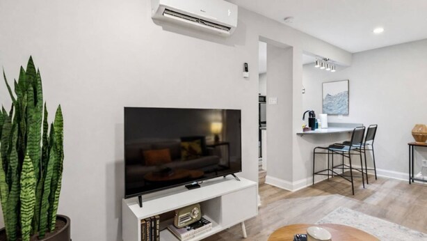 A modern living room with a flat-screen TV, a dining area with a table and chairs, and a potted plant. - September Savings:15% Off All 3+ Night Stays! (Charlotte)