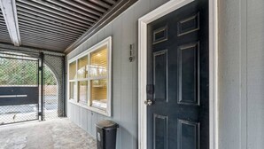 A garage entrance with a black door, a window with blinds, and a trash can. - September Savings:15% Off All 3+ Night Stays! (Charlotte)
