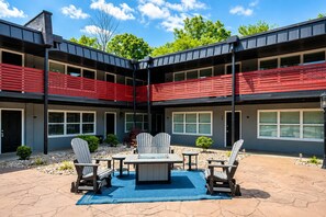 A two-story building with a covered outdoor patio area featuring a table, chairs, and a blue rug. - Modern & Cozy Oasis In Noda | Community Gym, Dog Park & Courtyard with Firepit | Pets OK! +20% Off! (Charlotte)