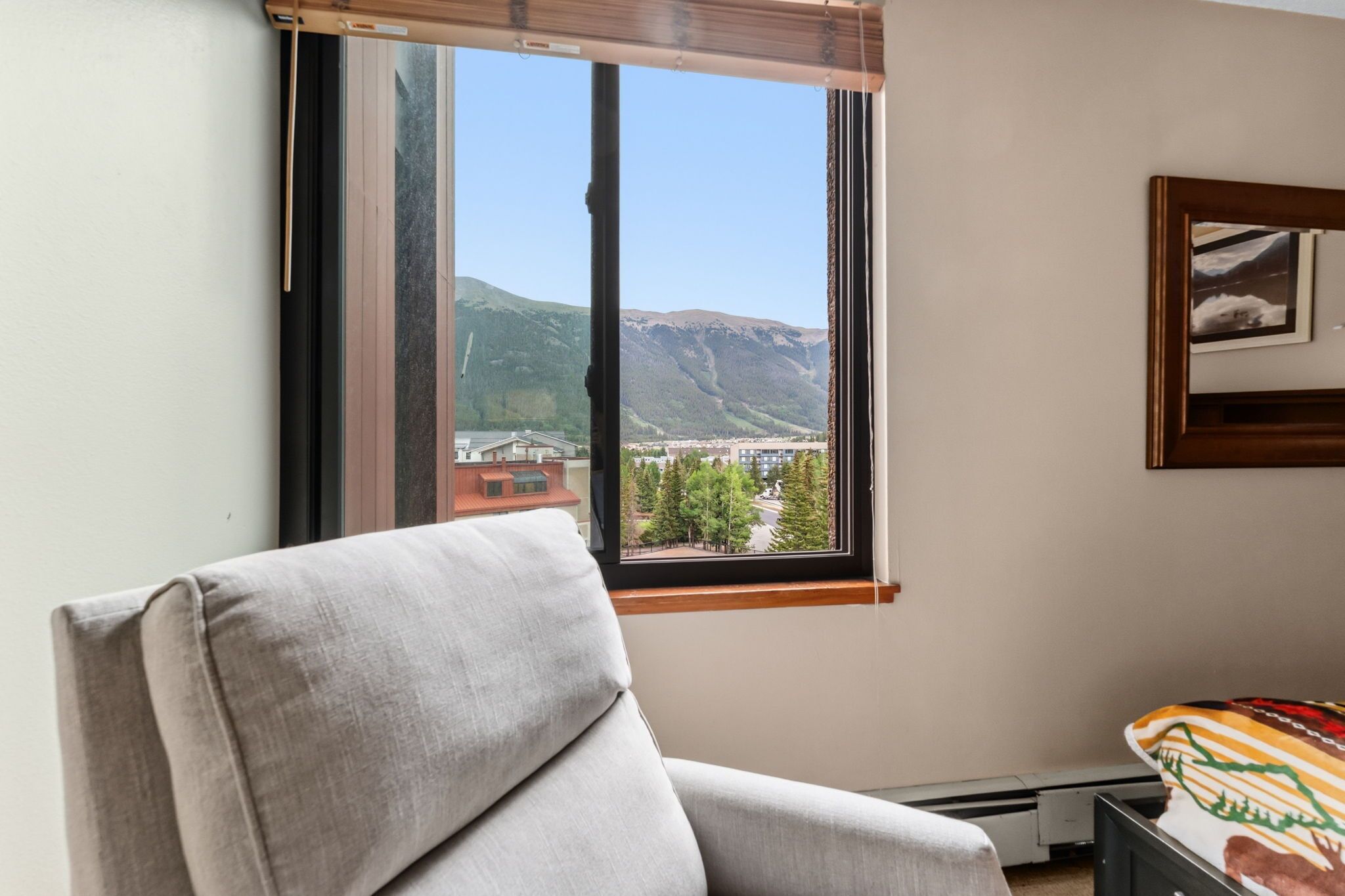 Una habitación con ventana que da a un paisaje montañoso, una silla y una cama con colcha estampada.