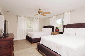 A hotel room with two beds, a ceiling fan, a TV on a dresser, and a window with curtains. - 4 BR Villa w/ Unique Layout Perfect f/ Large Group (Nassau)